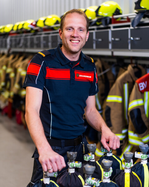 Lachende brandweerman in kazernekleding bij ademluchtflessen